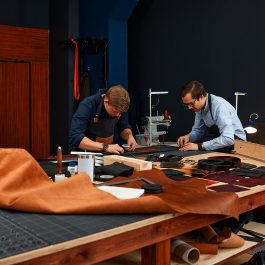 Two craftsmen working with leather and industrial tools on a large workshop table