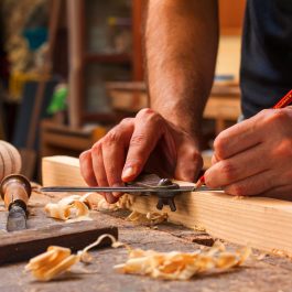 Craftsman marking wood with a marking gauge and pencil on a workshop bench