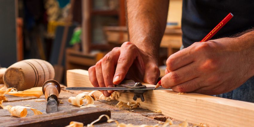 Craftsman marking wood with a marking gauge and pencil on a workshop bench