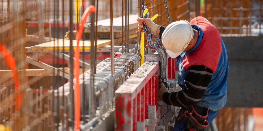 Construction worker in hard hat securing steel reinforcement bars on a job site