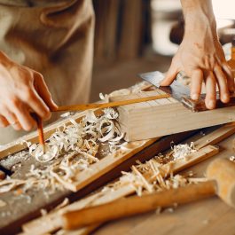 Carpenter using hand tools to plane and measure wood pieces on a workbench