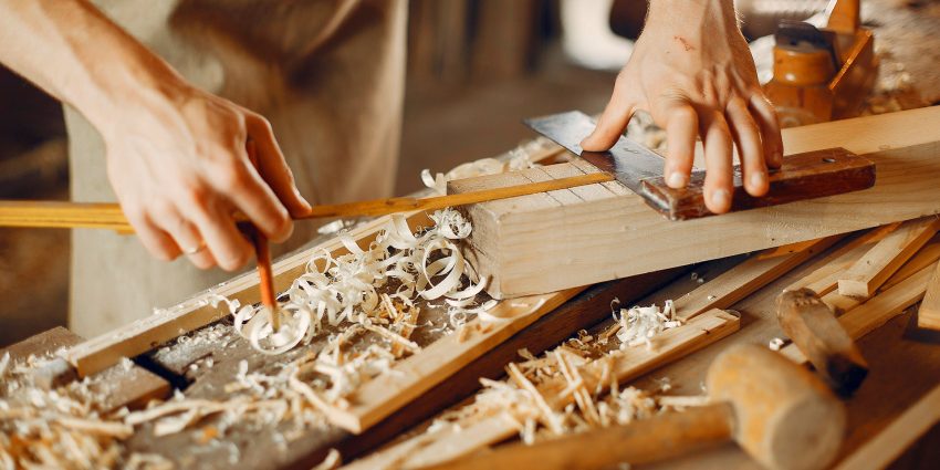 Carpenter using hand tools to plane and measure wood pieces on a workbench