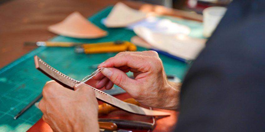 Hands hand stitching leather strap with saddle needles