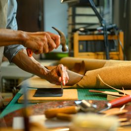 Craftsman hammering awl into leather on cutting mat
