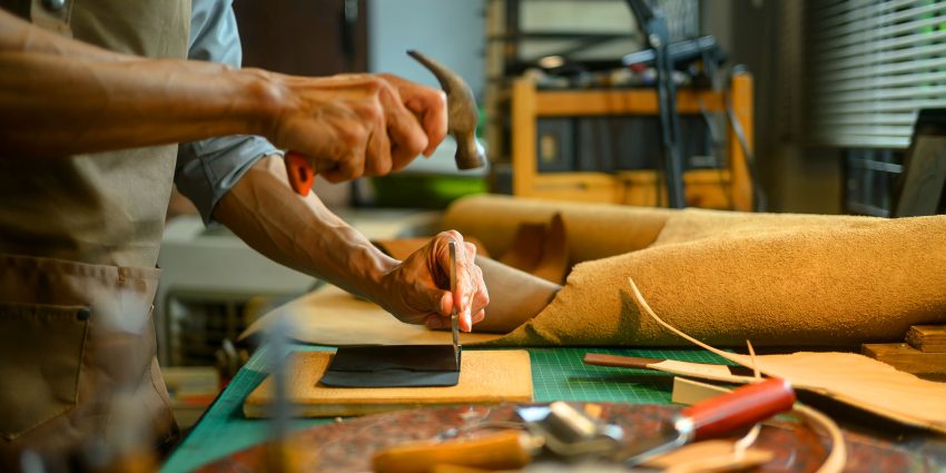 Craftsman hammering awl into leather on cutting mat